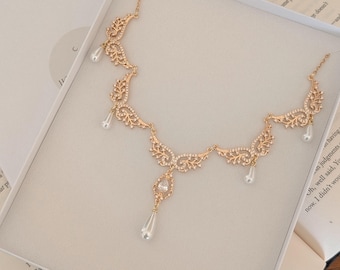 Puede incluir: Un collar dorado con un diseño de filigrana ornamentado, engastado con cristales transparentes y perlas de imitación en forma de lágrima. Presentado en una caja blanca, ideal para regalar.