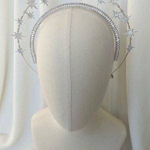 Puede incluir: Una diadema plateada con una doble fila de estrellas brillantes. Las estrellas est&aacute;n hechas de pedrer&iacute;a y est&aacute;n dispuestas en un patr&oacute;n circular.