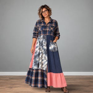 May include: A long-sleeved maxi dress featuring a navy and brown plaid bodice with a button-down front. The skirt combines panels of navy and white tie-dye fabric, solid navy fabric, and a solid coral pink hem, including a patch pocket.