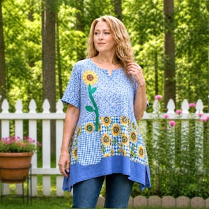 May include: A blue tunic top with a sunflower design. The top features a blue and white floral pattern on the upper portion, a gingham pocket, and a sunflower print on the lower portion. The tunic has short sleeves and a v-neck.
