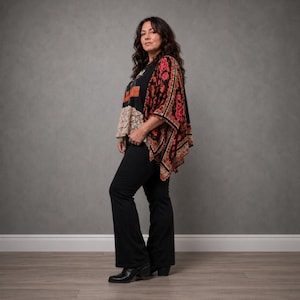 May include: A black graphic t-shirt with orange lettering and a beige lace hem, paired with a black kimono featuring a red and orange floral pattern. The outfit includes solid black flared trousers and black pointed-toe ankle boots.