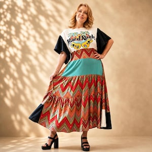 Könnte beinhalten: Eine Frau trägt ein farbenfrohes Kleid mit einem Hard Rock Cafe Grafik-T-Shirt. Das Kleid hat einen türkisfarbenen Mittelteil und einen gemusterten Rock mit roten, orangefarbenen und goldenen Zickzackmustern. Sie trägt schwarze Plateausandalen.
