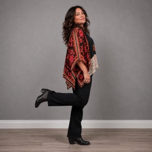 May include: A black top with a red and black floral patterned kimono-style overlay, paired with black trousers and black ankle boots. The kimono features a prominent red rose print with intricate black detailing and a wide, flowing silhouette.