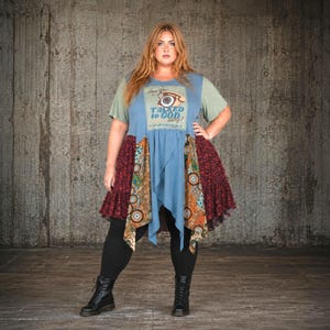 May include: A blue and green tunic top featuring a graphic of a vintage telephone with the text Talked to God lately? The garment has a layered hem with panels of floral and circular patterns in shades of maroon, orange, and brown, worn with black leggings.