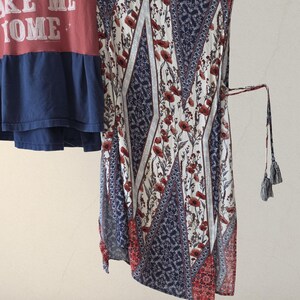 Pu&ograve; includere: Una maglietta rossa e blu con la scritta "MAKE ME HOME" e un vestito fantasia. L'abito presenta un motivo floreale con fiori rossi, motivi geometrici blu e bianchi e un fiocco con nappe.