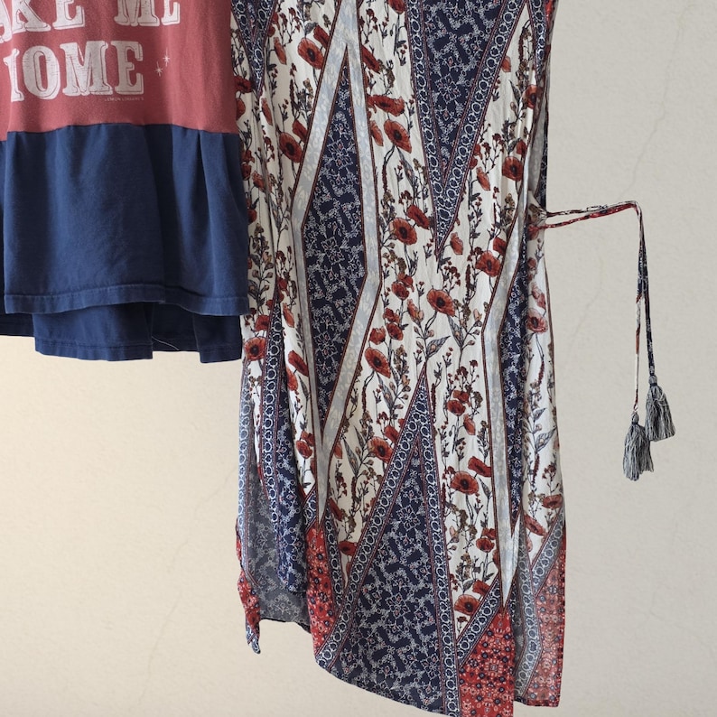 Pu&ograve; includere: Una maglietta rossa e blu con la scritta "MAKE ME HOME" e un vestito fantasia. L'abito presenta un motivo floreale con fiori rossi, motivi geometrici blu e bianchi e un fiocco con nappe.