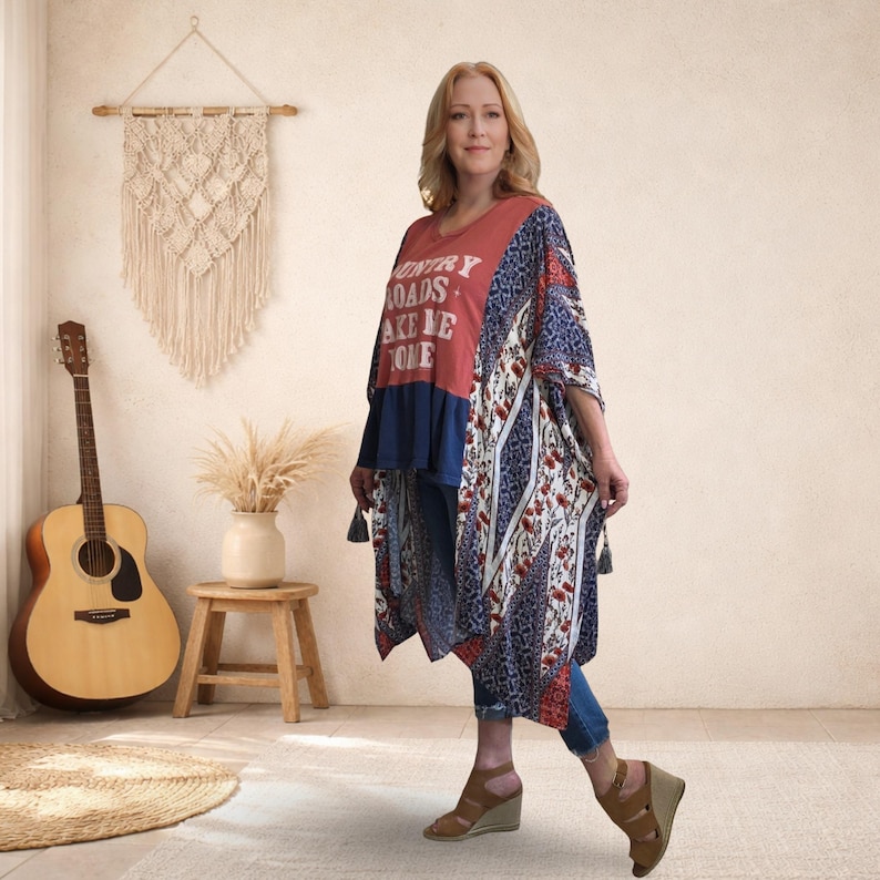 Pu&ograve; includere: Una donna indossa un top stile kimono rosso, blu navy e fantasia con la scritta "Country Roads Take Me Home". Il top &egrave; abbinato a jeans blu e sandali con zeppa marroni. Una chitarra e un arazzo in macram&egrave; sono sullo sfondo.