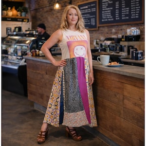 May include: A sleeveless patchwork dress featuring a Nirvana graphic on the top. The dress combines various fabric patterns, including floral, geometric, and solid colors. The model is wearing brown heeled sandals.