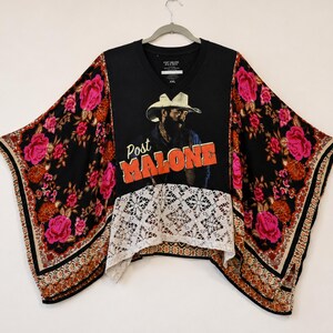 May include: A black V-neck top featuring a graphic of a person in a cowboy hat with the text Post MALONE in orange letters. The sleeves and lower back have a black floral pattern with pink roses, and the front hem features white lace trim.