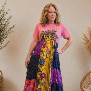 Op de afbeelding: Een roze T-shirt met de tekst "Fleetwood Mac" en een patchwork maxi-jurk. De jurk heeft bloemen- en geometrische patronen in geel, paars en blauw. De jurk is maxilengte.