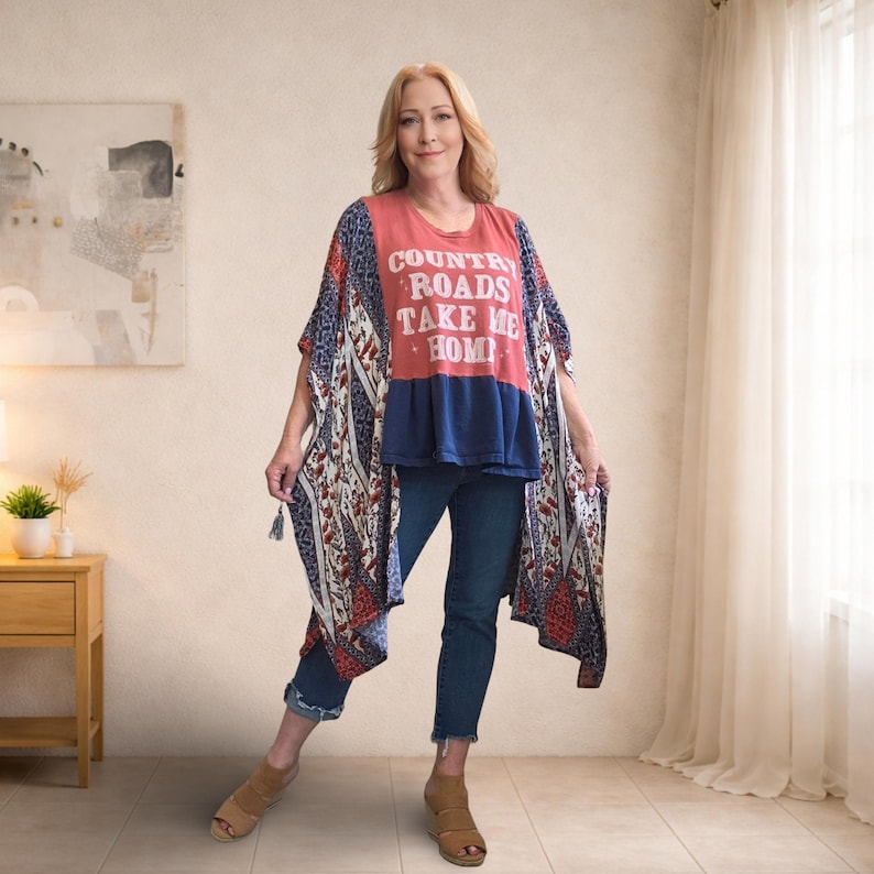 Pu&ograve; includere: Una donna indossa un kimono fantasia rosso, bianco e blu sopra una maglietta rossa con la scritta "COUNTRY ROADS TAKE ME HOME" e jeans blu. Il kimono ha nappe sulle maniche. Indossa sandali marroni.