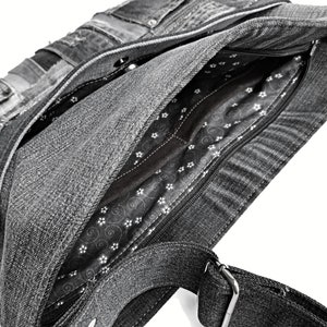 Puede incluir: Un bolso tote de mezclilla gris con cierre de cremallera y forro floral blanco y negro. El bolso tiene una correa larga ajustable.