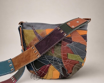 Puede incluir: Un bolso de hombro en forma de media luna hecho de parches de cuero multicolor en tonos verde oliva, amarillo mostaza, rojo oscuro, marrón y negro. El bolso presenta costuras blancas visibles y una correa de cuero ancha y multicolor.