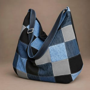 Könnte beinhalten: Eine Umhängetasche im Hobo-Stil, gefertigt aus einem Patchwork aus quadratischen Stoffbahnen in den Farben Schwarz, Hellblau-Denim, Dunkelblau-Denim und Grau. Die Tasche verfügt über einen langen, verstellbaren dunkelblauen Riemen mit einer silberfarbenen Metallschnalle.