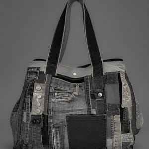 Könnte beinhalten: Eine Tragetasche aus einem Patchwork aus verschiedenen Grau- und Schwarztönen von Jeansstoff. Die Tasche verfügt über mehrere sichtbare Jeanstaschen, Metallnieten, Knopfverschlüsse und zwei robuste, schwarze Jeans-Schulterriemen oben.
