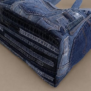 Może przedstawiać: Torba typu tote wykonana z przetworzonego niebieskiego dżinsu, charakteryzująca się patchworkowym wzorem w r&oacute;żnych odcieniach denimu, widocznymi szwami, postrzępionymi krawędziami oraz zintegrowanymi kieszeniami i prostokątną podstawą.