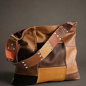 Puede incluir: Un bolso tipo hobo confeccionado con diversos parches de cuero en tonos marrón, beige y naranja. El bolso cuenta con una correa de hombro ancha y multicolor, decorada con remaches metálicos plateados en los bordes, creando un diseño de patchwork.