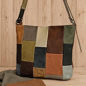 May include: A rectangular shoulder bag constructed from a patchwork of leather panels in various colors including brown, olive green, black, tan, and grey. The bag features a long adjustable strap and is accompanied by a matching tan leather wallet.