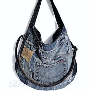 Peut inclure: Un sac cabas en jean bleu fabriqué à partir de jeans recyclés. Le sac a une fermeture éclair et une longue bandoulière. Le sac a un patch en cuir brun avec le texte "Recycled" dessus.