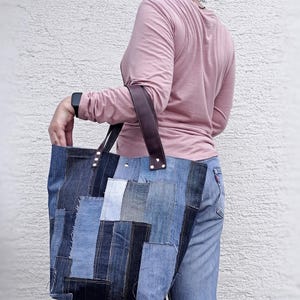 Op de afbeelding: Een grote denim tote bag gemaakt van patchwork denim in verschillende blauwtinten. De tas heeft bruine leren handvatten. De tas is een stijlvol accessoire voor het dragen van spullen.