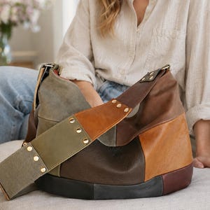 May include: A hobo bag constructed from multi-coloured leather panels in shades of olive green, tan, dark brown, and black. The wide shoulder strap features olive green leather accents secured with gold-toned metal rivets along the length.