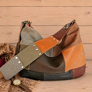 Puede incluir: Un bolso tipo hobo confeccionado con paneles de cuero multicolor en tonos marrón, beige, verde oliva y negro. La correa ancha para el hombro presenta remaches metálicos plateados y una sección de cuero gris texturizado, creando un diseño patchwork.