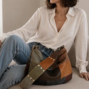 Può includere: Borsa a tracolla patchwork multicolore con un'ampia tracolla e borchie color oro. La borsa presenta pannelli marroni, verdi e beige. Il design della borsa suggerisce una costruzione artigianale, con una varietà di materiali e texture.