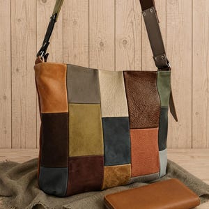 Könnte beinhalten: Eine Patchwork-Umhängetasche mit rechteckigen Feldern in den Farben Hellbraun, Olivgrün, Dunkelbraun, Creme, Marineblau und Rostorange, kombiniert mit einer passenden, einfarbigen hellbraunen Geldbörse mit umlaufendem Reißverschluss.