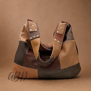 Puede incluir: Bolso de hombro de cuero patchwork en tonos marrón, beige y negro. El bolso presenta una correa ancha con detalles de remaches y una forma curva. El bolso tiene una gran capacidad y un estilo casual.