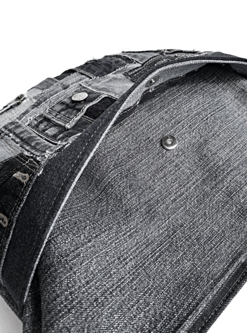 Puede incluir: Una bolsa de mano de lona negra con un dise&ntilde;o de patchwork. La bolsa est&aacute; hecha de lona reciclada y tiene un cierre magn&eacute;tico.