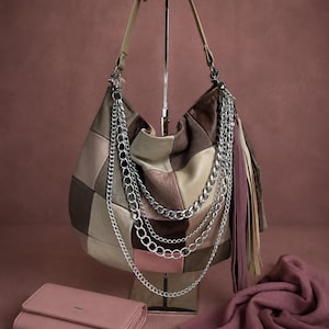 Puede incluir: Un bolso hobo de patchwork con paneles de cuero en tonos marrón, beige y rosa, decorado con varias cadenas de metal plateado y largos flecos de cuero. Se incluyen una cartera rectangular rosa a juego y una bufanda de color rosa.