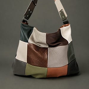 May include: A hobo-style shoulder bag constructed from a patchwork of textured leather panels in shades of dark green, cream, chocolate brown, light gray, olive green, and terracotta, featuring a wide strap attached with silver-toned metal rivets.