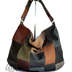 Puede incluir: Un bolso de hombro patchwork en varios tonos de marrón, verde y gris. El bolso presenta un diseño grande y holgado con una correa ancha. El bolso de cuero se muestra sobre un fondo blanco.
