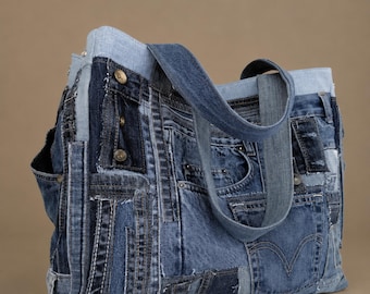 May include: A tote bag constructed from various shades of blue denim fabric patches. The bag features multiple visible pockets, metal buttons, and stitched seams from repurposed jeans. It includes two denim shoulder straps and a light blue trim.