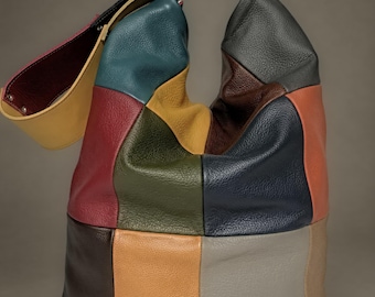 Puede incluir: Un bolso tipo hobo confeccionado con paneles de cuero texturizado multicolor en tonos azul verdoso, amarillo, verde oliva, marrón oscuro, azul marino, naranja, gris y beige. El bolso cuenta con una correa ancha ajustable con herrajes plateados.