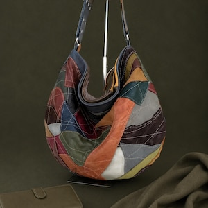 Op de afbeelding: Een hobo-schoudertas gemaakt van veelkleurige leren patches in tinten bruin, rood, blauw, groen, grijs en wit. De tas is voorzien van zichtbare contraststiksels over het hele patchwork-ontwerp en een enkele leren schouderband.