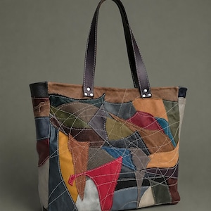 Puede incluir: Un bolso tote confeccionado con parches de cuero multicolor en tonos rojo, amarillo, azul, verde, marrón y negro. El exterior presenta costuras blancas en contraste sobre el diseño de patchwork y dos correas de hombro de cuero marrón oscuro.