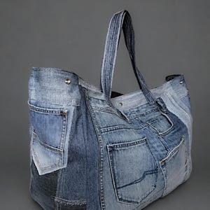 Könnte beinhalten: Eine große Tragetasche aus verschiedenen Blautönen von Jeansstoff. Die Außenseite ist mit mehreren aufgesetzten Taschen, sichtbaren Nähten und Metallnieten versehen. Sie verfügt über zwei robuste Jeansgriffe und eine Öffnung mit Druckknopf.