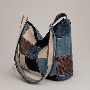 Könnte beinhalten: Eine Schultertasche im Hobo-Stil aus einem Patchwork aus blauem Denim, braunem strukturiertem Stoff und schwarzen Einsätzen. Die Tasche verfügt über einen breiten, beigen Canvas-Riemen mit sichtbaren Nähten und einen schwarzen Reißverschluss.