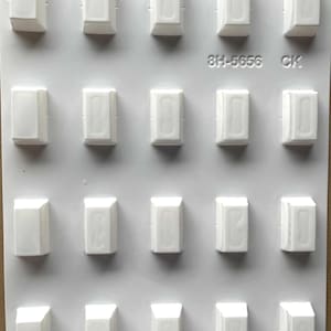 May include: A white plastic mold with 20 rectangular cavities. Each cavity has a slightly angled top and a vertical indentation. The mold has the text "8H-5656 CK" printed on it.