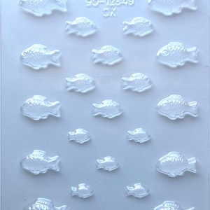 May include: Clear plastic mold with various sizes of fish shapes. The mold has the text "90-12849 CK" printed at the top. The fish shapes are detailed with fins and scales, perfect for crafting or baking.