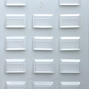 May include: A clear plastic mold with twelve rectangular cavities. The mold has the text "90-5023" and "Approx. 60 Pieces per Pound". The mold is designed for creating small, rectangular items.