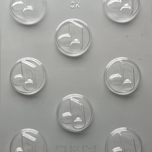 May include: Clear plastic mold with nine circular cavities, each featuring a raised musical note design. The mold has the text "90-13905 CK" and "FITS BOX 87-13!" printed on it. The mold is designed for creating themed treats.