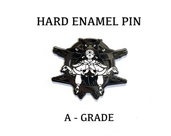 Könnte beinhalten: Schwarze und weiße Emaille-Anstecknadel mit einer Figur mit mehreren Augen, umgeben von Raben. Die Anstecknadel trägt die Aufschrift "HARD ENAMEL PIN" und "A - GRADE".