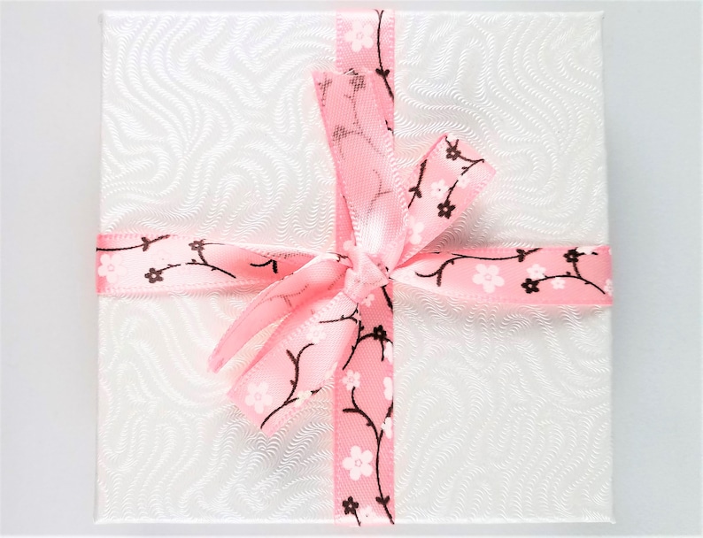 May include: A white gift box with a pink ribbon tied in a bow. The ribbon has a pattern of brown branches with pink flowers.