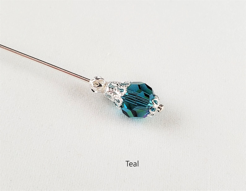 May include: Teal crystal bead with silver filigree accents on a silver pin.