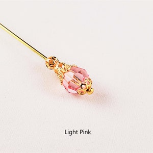 May include: A gold pin with a light pink glass bead. The bead has a gold filigree design around it. Light Pink.