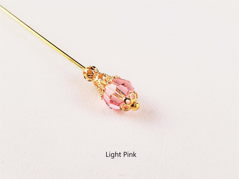 May include: A gold pin with a light pink glass bead. The bead has a gold filigree design around it. Light Pink.
