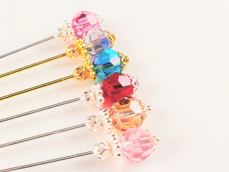 May include: Six decorative pins with colorful crystal beads and gold or silver accents. The beads are pink, clear, teal, red, amber, and pink.