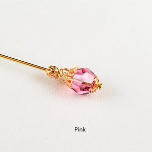 May include: A gold pin with a pink faceted glass bead and a gold filigree design. The pin is on a white background. Pink.
